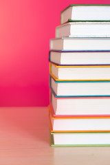 Stack of colorful books, bright colorful pink background, free copy space. Books on table, no labels, blank spine. Back to school. Education background