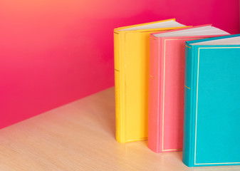 Simple composition of hardback multicolored books, raw of books on pink background. Books stacking with no labels, blank spine Back to school Copy Space Education background Office supplies