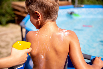 Parent applying sunblock cream on son shoulder, sun protection