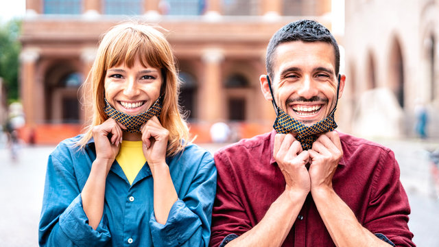 Happy couple smiling with opened face mask after lockdown reopening - New normal relationship concept with guy and girl having fun together on travel experience - Vivid filter with selective focus