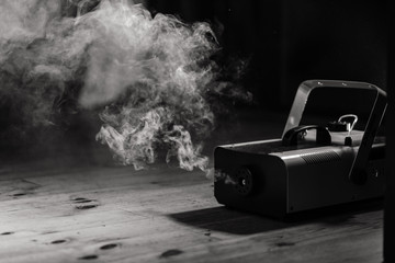 Smoke coming from the smoke machine standing on the floor. Black and white background