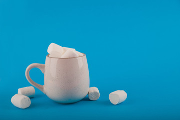 Marshmallows in a mug on a blue background close-up and copy space. Marshmallow in a cup pattern top view on a blue background.