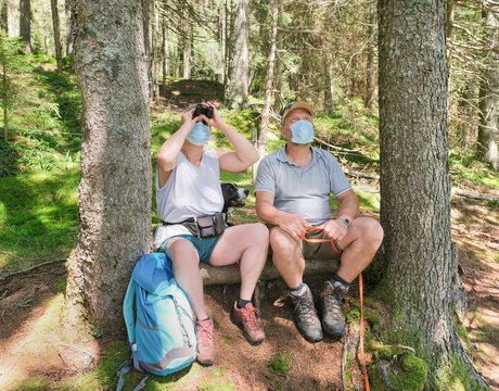Senior couple have a rest in a forest while wearing protective face mask and watch something with the binoculars - Health care and coronavirus lifestyle
