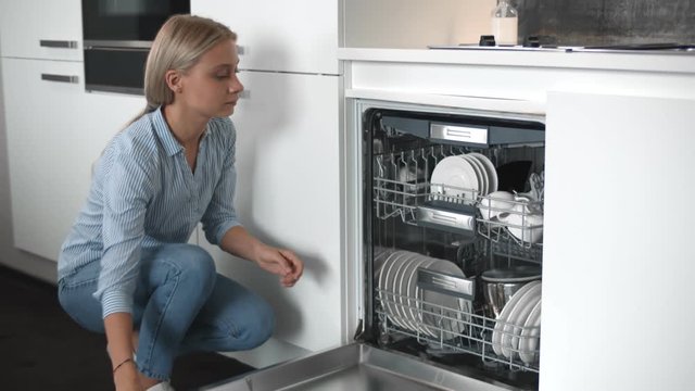 Young Beautiful Woman Unloading Dishes From Dishwasher Machine.