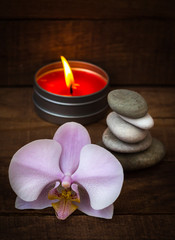 Spa stones with a pink Orchid and a burning scented candle on a brown wooden background