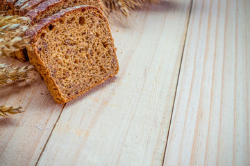 Rustic bread. Fresh loaf of rustic traditional bread with wheat grain ear or spike plant on wooden texture background. Rye bakery with crusty loaves and crumbs. Concept - Cooking at Home.