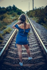 Beautiful attractive woman with long hair in blue dress on the old railroad. Backview image.