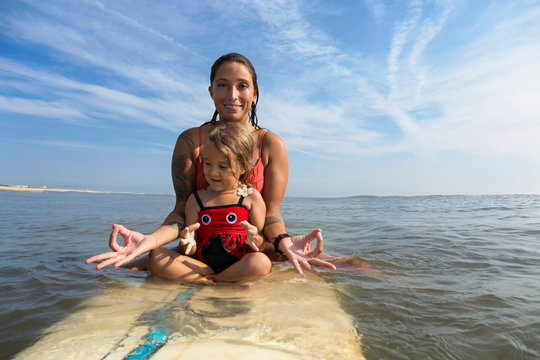 Mother and daughter meditating on surfboard - Powered by Adobe