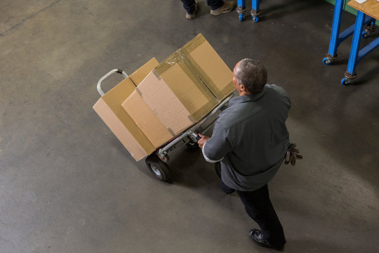 Worker carting boxes on hand truck in warehouse