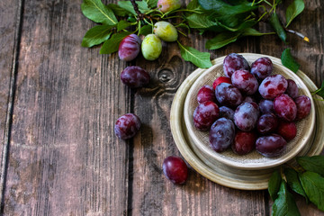 Ripe juicy plums in a bowl on a wooden background. Copy space.