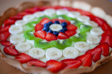Crostata di frutta fatta in casa con fragole, mirtilli, kiwi, banane e crema pasticciera. Focus su dettagli, colori, dimensioni e fondo di biscotto.