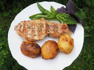 Golden-crusted potatoes with pork steak with a Basil leaf on a plate. the food is cooked on the grill.