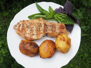 Golden-crusted potatoes with pork steak with a Basil leaf on a plate. the food is cooked on the grill.