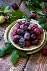 Ripe juicy plums in a bowl on a wooden background.
