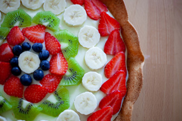 Crostata di frutta fatta in casa con fragole, mirtilli, kiwi, banane e crema pasticciera. Focus su dettagli, colori, dimensioni e fondo di biscotto.