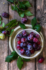 Ripe juicy plums in a bowl on a wooden background.