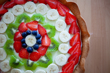Crostata di frutta fatta in casa con fragole, mirtilli, kiwi, banane e crema pasticciera. Focus su dettagli, colori, dimensioni e fondo di biscotto.