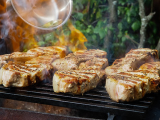 a man pours alcohol on the meat on the grill. roasting steaks on the fire. flambé.flamber.