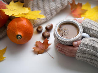 A woman in a knitted sweater holds a Cup of hot aromatic espresso coffee on the windowsill. Autumn time and mood. Yellow maple leaves and pumpkin