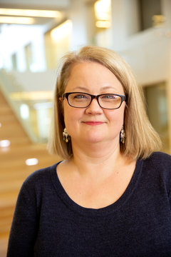 Portrait of middle aged woman wearing glasses standing by stairwell in lobby of building, smiling looking towards camera 