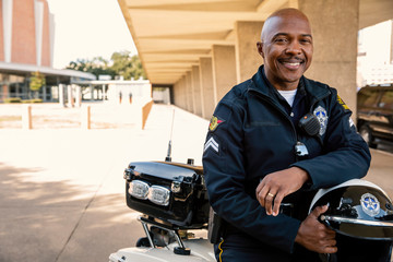 Portrait of Police officer sitting on his motorcycle outside looking towards camera smiling 