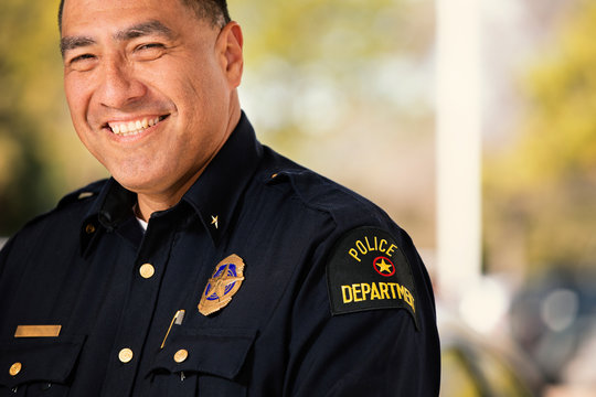 Portrait of Police officer standing outside with arms crossed looking towards camera smiling 