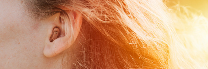 small intra channel hearing aid in the ear of a woman. banner. flare