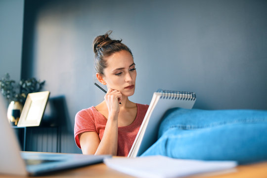 Businesswoman With Note Pad And Pencil Relaxing At Desk In Home Office