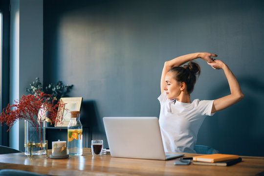 Tired Businesswoman Stretching Arms While Sitting At Desk In Home Office