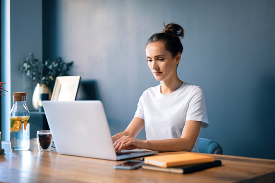 Confident businesswoman using laptop on desk against wall in home office