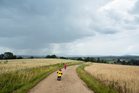 Girls with bicycle and balance bicycle on dirt track, rain clouds