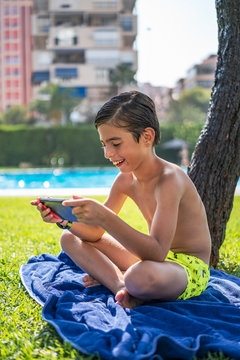 Shirtless boy playing video game over digital tablet while sitting on towel in yard