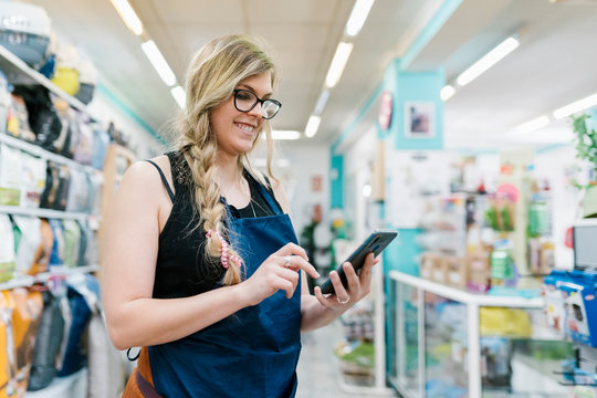 Smiling Female Groomer Using Smart Phone While Standing In Pet Salon