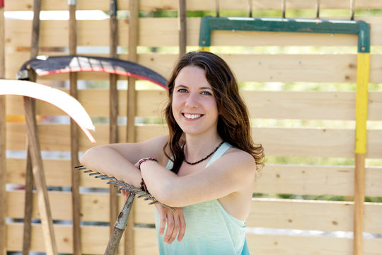 Smiling beautiful woman with gardening equipment standing against fence