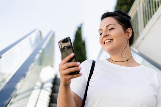 Smiling curvy young woman using mobile phone on escalator - Powered by Adobe