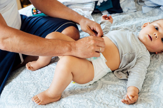 Father with baby boy lying on bed, changing diapers