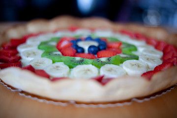 Crostata di frutta fatta in casa con fragole, mirtilli, kiwi, banane e crema pasticciera. Focus su dettagli, colori, dimensioni e fondo di biscotto.
