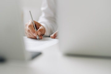 Close-up of female entrepreneur writing on paper at desk in home office