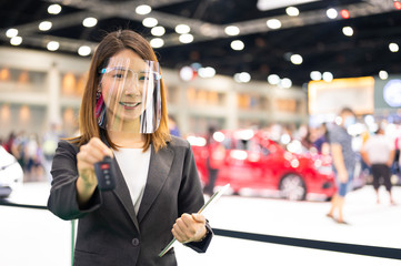 Asian car seller wearing face mask presents car and passing new car key to customer after purchased while coronavirus pandemic