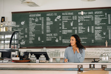 Female owner using digital tablet looking away while standing at counter in cafe