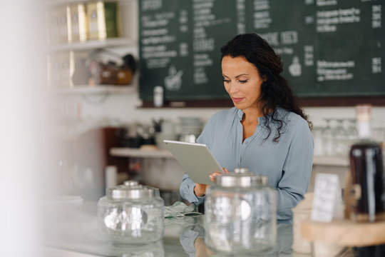 Mid adult woman using digital tablet while standing at counter in coffee shop
