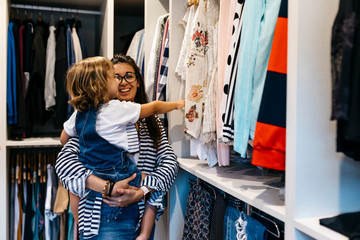 Happy mother carrying daughter choosing clothes in dressing room at home