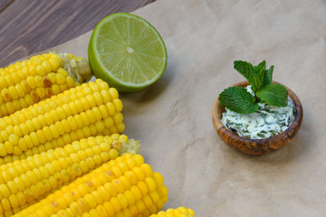 Butter with herbs and salt in a wooden plate and sweet corn on craft paper. Delicious mint corn sauce. Closeup.