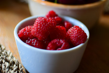 Raspberries in a ceramic bowl on a wooden table.