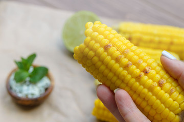 Young yellow fried sweet corn in the girl's hand. Delicious summer food. Close-up.