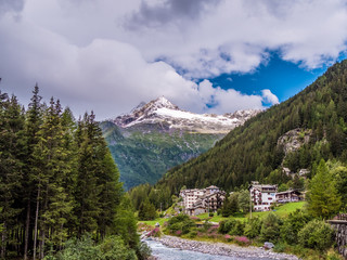 Der kleine Ort Chiareggio mit dem Fluss Torre Malenco im Valmalenco mit schneebeckten Bergen bei...