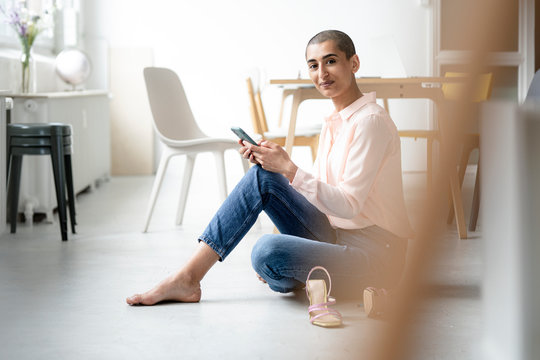 Portrait of woman sitting on the floor in a loft holding smartphone