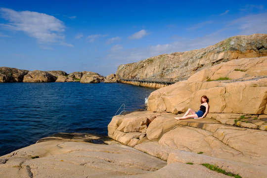 Teenage girl relaxing on rocky shore in summer