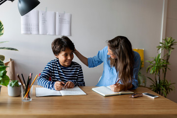 Female tutor talking with smiling boy while sitting at table