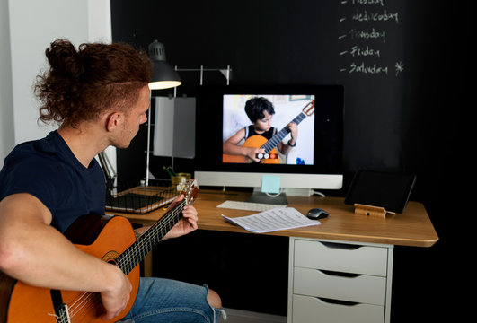 Man Learning Guitar While Watching Tutorial At Home